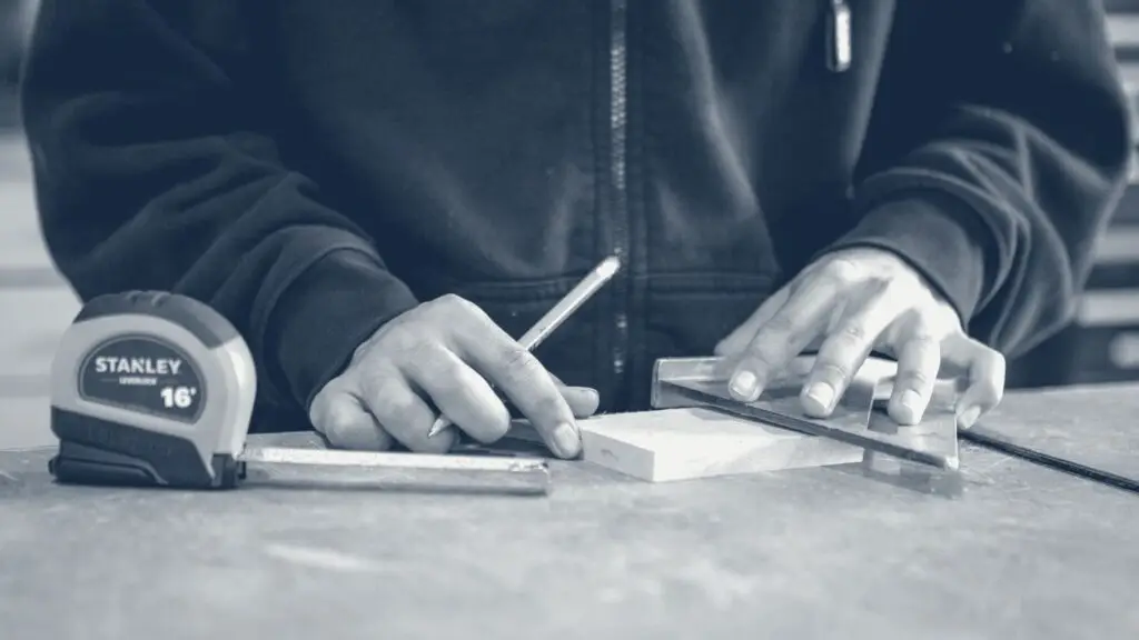 Mains d'artisan traçant une mesure au crayon sur une planche de bois