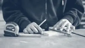 Mains d'artisan traçant une mesure au crayon sur une planche de bois